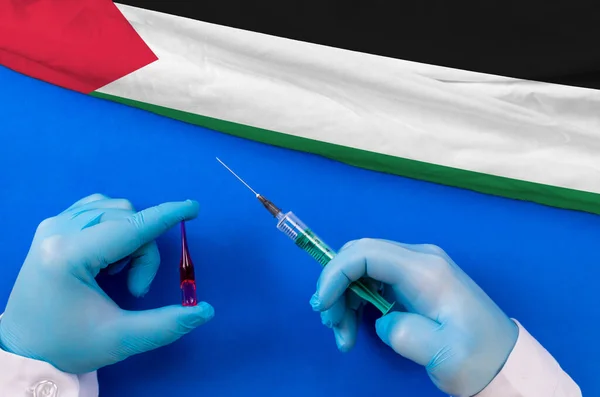 Palestine Vaccination. Hands of doctor holding syringe and coronavirus (COVID-19) vial vaccine on flag Palestine