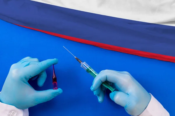 Russia Vaccination. Hands of doctor holding syringe and coronavirus (COVID-19) vial vaccine on flag Russia