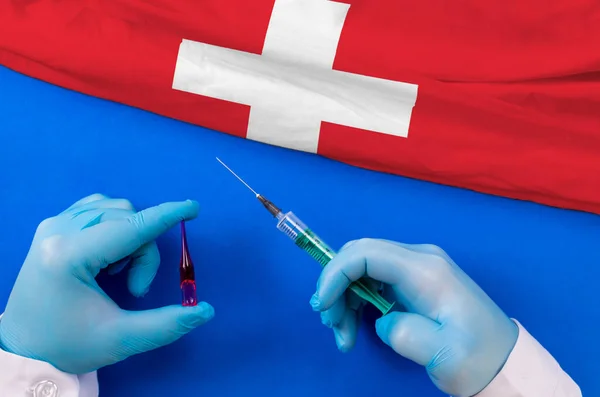 Switzerland Vaccination. Hands of doctor holding syringe and coronavirus (COVID-19) vial vaccine on flag Switzerland