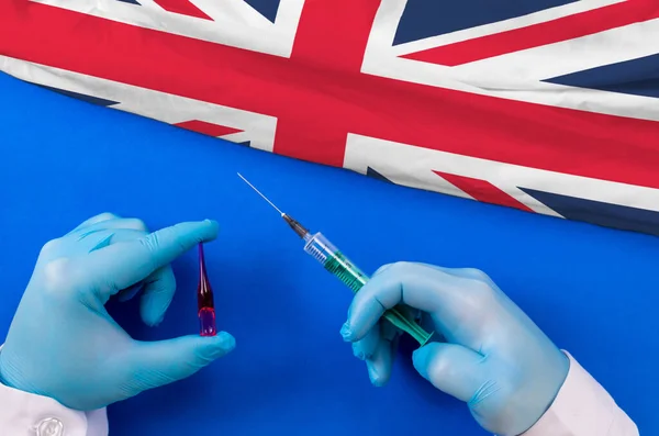 United Kingdom Vaccination. Hands of doctor holding syringe and coronavirus (COVID-19) vial vaccine on flag United Kingdom