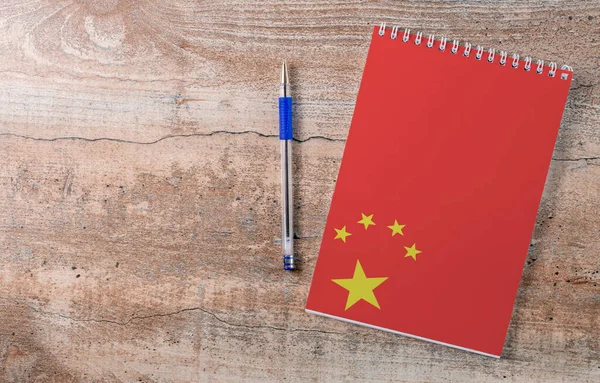 Notepad with China flag, pen on wooden background, study concept