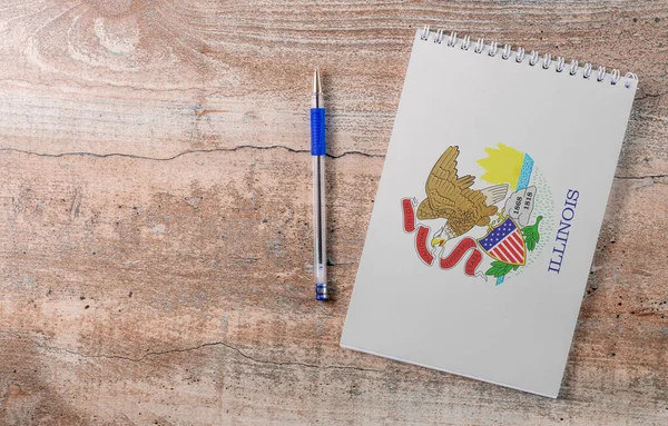 Notepad with Illinois flag, pen on wooden background, study concept