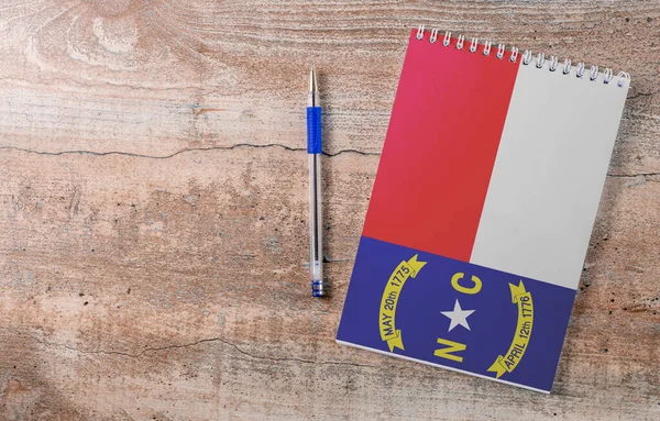 Notepad with North Carolina flag, pen on wooden background, study concept
