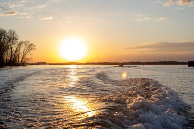 Gün batımında nehirdeki motordan gelen dalgalar