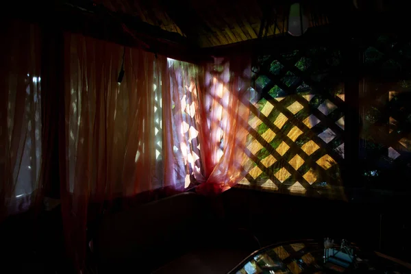 Renkli ışık perdeleri olan gölgeli yaz çardağı. Karanlıktaki ahşap çardak kafe.