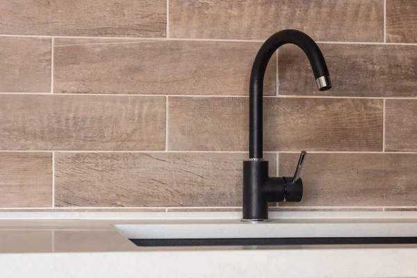 black faucet in the kitchen on the background of tile in the form of a brick