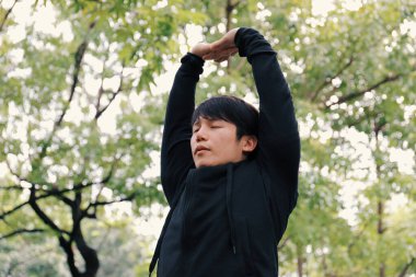 Genç Asyalı sağlıklı bir adam park, egzersiz ve spor antrenmanı konseptinde ısınıp ısınıyor.