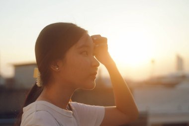 Genç Asyalı genç kız gün batımını seyrediyor. Gökyüzü, duygusal duygu, sakin ve huzurlu bir geçmiş. 