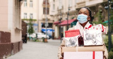 Güzel Afrikalı Amerikalı kadın Noel alışverişinden sonra bir sürü hediye kutusuyla süslü şehirde yürüyor. Maskeli mutlu bir bayanın portresi bayram hediyeleri içeriyor. Sürpriz hediye konsepti