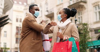 Tıbbi maskeli neşeli Afro-Amerikan genç adam ve kadın portresi Noel alışverişinden sonra sokakta toplanıyor ve kar yağarken kibarca konuşuyorlar. Dirseklerle selamlaşan arkadaşlar