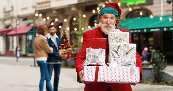 混雑した通りに立っているサンタクロースの衣装で幸せなシニア白人男性の肖像画や多くのクリスマスプレゼントを保持し 親切に笑顔 休日の精神 クリスマスのコンセプト — ストック写真
