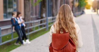 Fotokopi kitaplarıyla sokakta yürüyen ve arkadaşlarına el sallayan Kafkasyalı mutlu öğrenci kızı. Sırt çantalı güzel bir kız öğrenci okula gidiyor. Kapatın. Eğitim kavramı