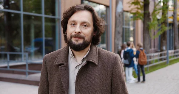 Portrait of joyful handsome man in good mood standing near college and smiling to camera outdoors. Male teacher posing with happy face while standing on street. Bearded proffesor. Tutor concept — Stock Photo, Image