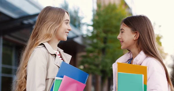 Primer plano retrato de alegre hermosa niñas estudiantes de la escuela con copybooks charlando mientras está de pie en la calle de buen humor. Caucásico bastante feliz mujer adolescente amigos hablando concepto de amistad —  Fotos de Stock