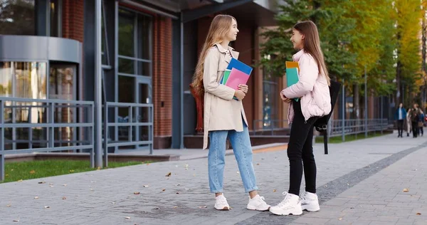 Χαρούμενα όμορφα νεαρά κορίτσια μαθητές σχολείου με πολύχρωμα copybooks μιλώντας ενώ στέκεται στο δρόμο σε καλή διάθεση. Καυκάσιες, χαρούμενες έφηβες μαθήτριες μιλάνε. Έννοια φιλίας — Φωτογραφία Αρχείου