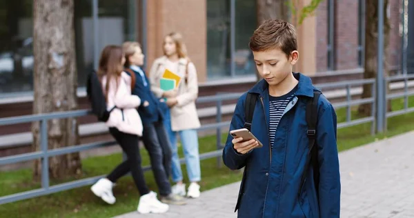 행복 한 학생이 학교로 걸어가고 휴대폰으로 타자를 치는 모습입니다. 남자 아이가 집 밖에서 급우들에게 손을 흔들어 줍니다. 학생들이 스마트폰으로 문자를 보내고 도청을 합니다. 레저 개념 — 스톡 사진