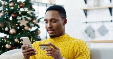 Mutlu adamın mutlu yüz ifadesiyle online olarak akıllı telefondan Xmas satışı yaptığı yakın plan portresi. Neşeli adam internet üzerinden noel hediyesi alıyor ve kredi kartıyla ödüyor. Yeni yıl konsepti