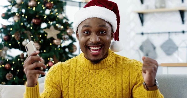 Close up of African American joyful surprised excited man receiving great news on smartphone about lottery win on Christmas Eve Guy feeling happy having unbelievable luck happy emotions New Year sales