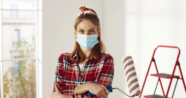 Primer plano retrato de la joven mujer caucásica feliz en la máscara de pie en el nuevo apartamento vacío sala de renovación de la celebración de rodillo de pincel de pintura en la mano renovando el hogar. Concepto de reparación. Decoración y reparación —  Fotos de Stock