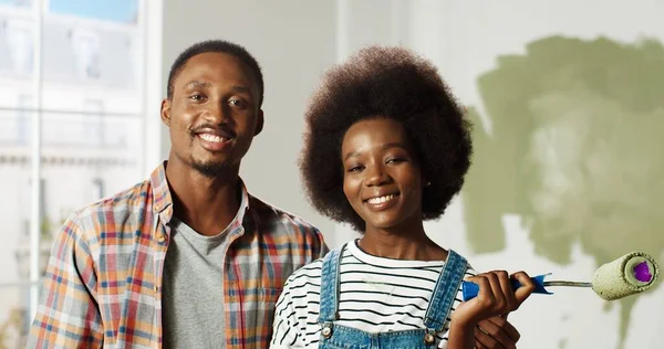 Close up retrato da alegre família afro-americana casal esposa e marido ficar no quarto durante a renovação da casa sorrindo para a câmera. Conceito de reparação e melhoria da casa. Decoração de paredes — Fotografia de Stock