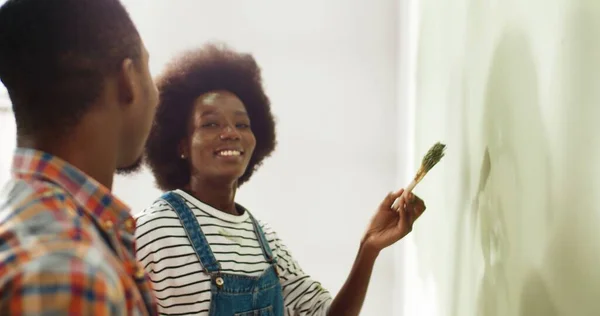 Närbild av happu gift ung afroamerikansk fru och make måla väggar i lägenhet med pensel och ha kul, skratta och måla på varandras ansikten. Hemreparationskoncept — Stockfoto