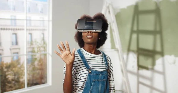 Nahaufnahme einer jungen Afroamerikanerin, die mit einer VR-Brille im Haus steht und mit den Händen in der Luft blättert, um moderne Innovationen zur Reparatur und Verbesserung ihres Zuhauses zu nutzen. Virtual-Reality-Technologie — Stockfoto