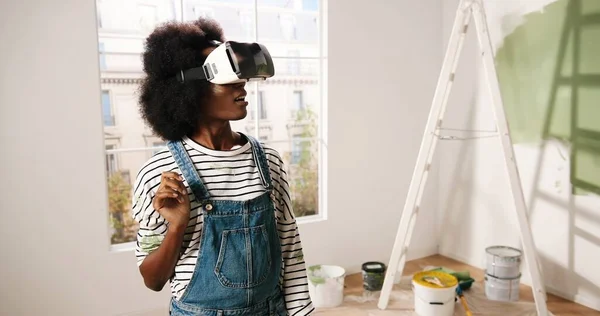 Retrato de afro-americano jovem impressionado mulher animado fica no quarto vestindo óculos VR e olhando para o novo apartamento renovado redesenhado usando inovações modernas e tecnologia de realidade virtual — Fotografia de Stock