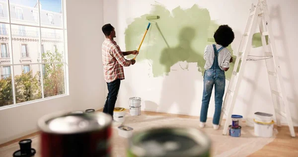 Baksidan av ung härlig afroamerikansk familj gift par gör renovering arbeten i huset. Fru och make måla väggar tillsammans med hjälp av rullborstar inredning och omformning hem — Stockfoto