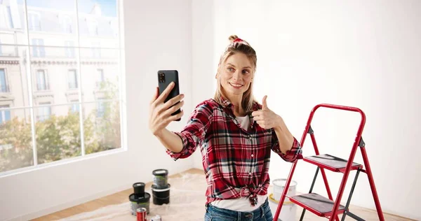 Mujer caucásica bastante alegre tomando fotos selfie en el teléfono móvil solo en el estado de ánimo positivo en la habitación durante el proceso de renovación. Mujer posando para fotos en smartphone. concepto de reparación del hogar — Foto de Stock