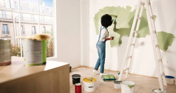Mladá Afroameričanka sama malovat stěnu s válečkem štětcem v olivové barvě při renovaci bytu. Zadní strana ženy redekorace domů, renovace a zlepšení koncepce oprav a zdobení — Stock fotografie