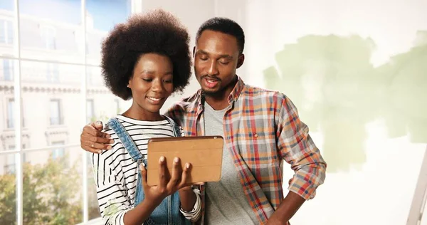 Afro-Amerikaanse jonge vrouw en echtgenoot paar tikken en browsen op tablet apparaat kiezen decoratie ideeën voor nieuwe appartement bespreken herontwerpen huis. Reparatie en verbetering van woningen — Stockfoto