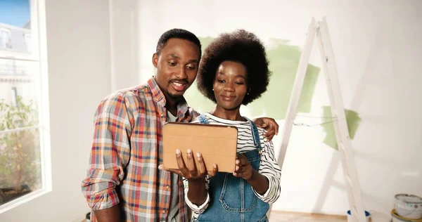 Afroamericano giovane moglie e marito coppia toccando e navigando sul dispositivo tablet scegliendo idee di decorazione per il nuovo appartamento discutendo ridisegnare casa. Riparazione e miglioramenti a casa — Foto Stock