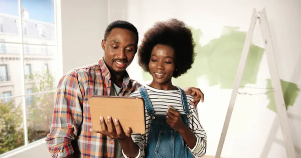 Afroameričtí mladí manželka a manžel pár klepání a prohlížení na tablet zařízení výběru dekorace nápady pro nový byt diskutovat o redesignu domu. Domácí opravy a vylepšení — Stock fotografie