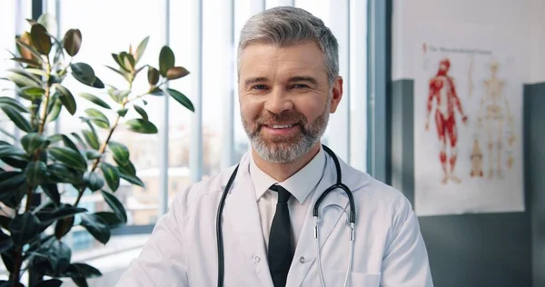 Close up ritratto di felice bello caucasico di mezza età esperto medico di sesso maschile in camice bianco guardando la fotocamera e sorridente in armadio in ospedale sul posto di lavoro, uomo infettante, concetto di assistenza sanitaria — Foto Stock