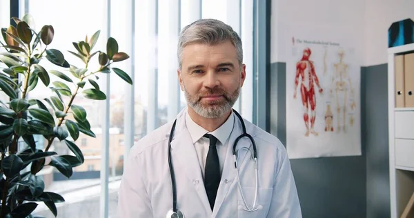 Ritratto ravvicinato del bel caucasico anziano gioioso medico infettante in camice bianco seduto nell'armadietto in clinica al lavoro che parla in videochiamata online tramite webcam con concetto di medico paziente — Foto Stock