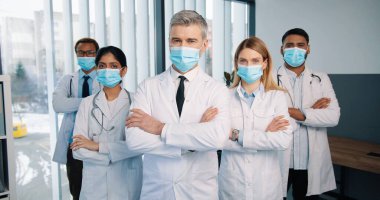 Klinikte kameraya, karantina konseptine, takım arkadaşlarına bakarak poz veren farklı ırktan farklı sağlık görevlilerinin, doktor ve doktorların portresi.