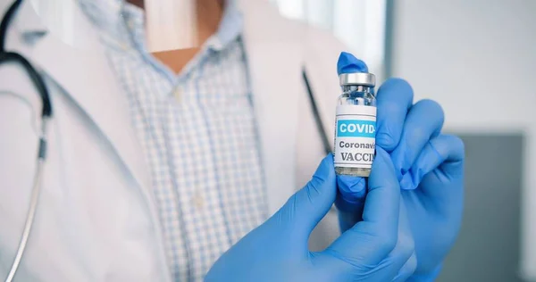 Close up skud af sundhedspersonale specialist i beskyttende uniform bedrift i hænder i handsker ampul med coronavirus vaccine, covid-19 vaccination koncept, virus kur medicin, sundhedspleje - Stock-foto