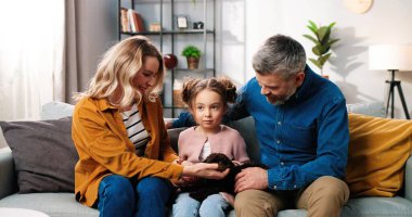 Beyaz, mutlu, şefkatli bir aile babası. Oturma odasındaki kanepede oturan anne ve baba. Küçük sevimli bir kız çocuğu ve evcil bir köpek yavrusu.