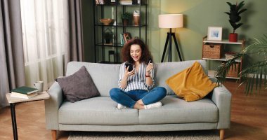 Kafkasyalı neşeli genç bayan internet üzerinden akıllı telefon alışverişi yapıyor. İnternetten kredi kartıyla iyi bir e-ticaret alışverişi yapıyor. Cep telefonuyla rahat bir odada oturuyor.