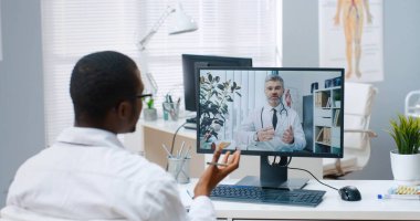 İnternet üzerinden Afrikalı Amerikalı erkek uzman konuşmalarının omuz hizasında bilgisayardaki orta yaşlı beyaz doktorla internet konferansındaki deneyimli hekim danışmanları