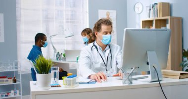 Kafkasyalı orta yaşlı doktor portresi. Klinikte çalışan bir bilgisayar uzmanı. Kadın meslektaşı Afrikalı Amerikalı bir hastayla arka plan hastane konseptini konuşuyor.