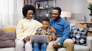 Genç, güzel, Afro-Amerikan bir ailenin bilgisayar kullanarak evdeki kanepede birlikte vakit geçirmesi. Anne ve baba kanepede oturmuş oğluyla internette yazı yazıyor, internette eğitim görüyor.