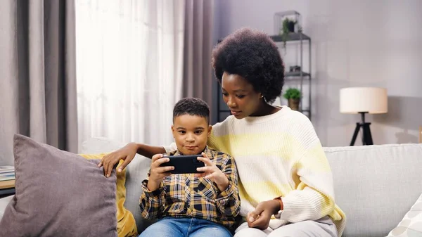 Genç anne ve babasıyla kanepede otururken akıllı telefondan yazı yazan tatlı Afro-Amerikan çocuk portresi. Teknoloji aleti, cep telefonu uygulaması, çocuk konsepti