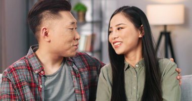 Evdeki rahat odada kanepede otururken kocasıyla konuşan mutlu Asyalı genç bir kadın. Mutlu ve evli bir çift, evde mutlu bir şekilde vakit geçiriyorlar.