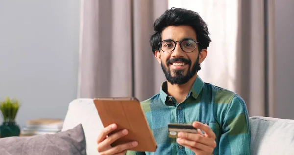 Retrato de indio joven barbudo feliz hombre en gafas de compras en línea de compra en Internet utilizando el dispositivo de la tableta haciendo el pago con tarjeta de crédito, servicio de comercio electrónico, shopaholic comprador concepto — Foto de Stock
