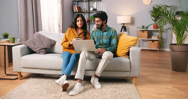 Hindu glad glad glad glad ung gift par sitter på soffan i moderna rum surfa på bärbar dator köpa göra inköp med kreditkort, internet shopping, familj tid, e-handel koncept — Stockfoto