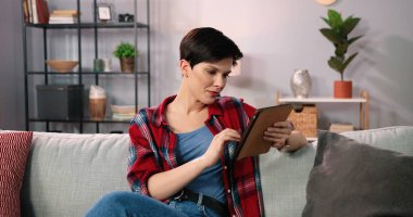 Kanepede dinlenirken internetten alışveriş yapan bir kadın. Harcayacak kadar nakitim var. Mutlu esmer kadın çevrimiçi ödeme yapmak için kredi kartını kullanıyor. Kamera görünümü kavramını yakınlaştır