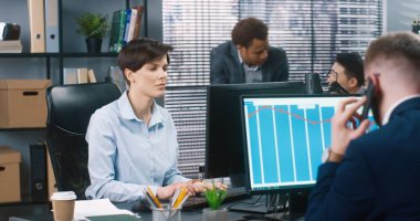 İş yerindeki ofis çalışanları. Beyaz tenli güzel kadın çalışan dolapta bilgisayarda yazarken, erkek akıllı telefondan konuşuyor. Arkada çalışan melez erkekler. Meslek kavramı