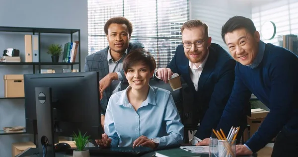 年轻快乐的多民族专业企业家团队的画像，他们在办公室工作，看着相机，面带微笑。男人站在漂亮的女同事旁边，打字在电脑上，在工作观念上 — 图库照片