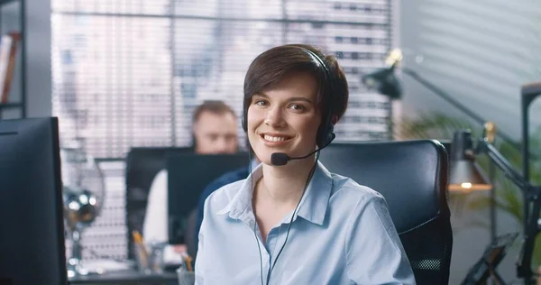 Närbild porträtt av glada unga kaukasiska vackra kvinnliga call center operatör sitter vid skrivbord i skåp i headset tittar på kameran och ler. Glädjande kvinna anställd på jobbet, arbetstagare koncept — Stockfoto